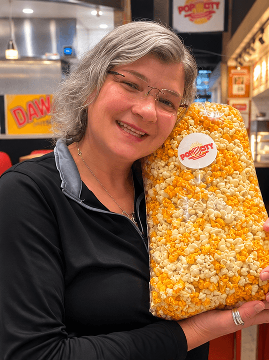 A smiling supporter holding a tall bag of Pop City popcorn